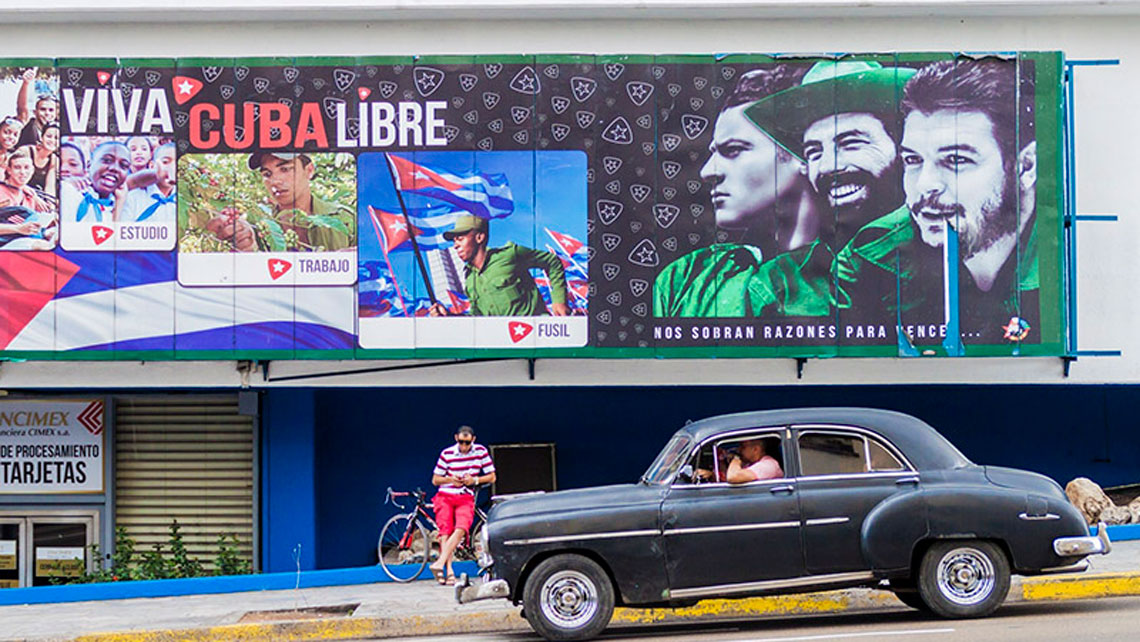 A vintage american car passing by a wall full of Revolution messages