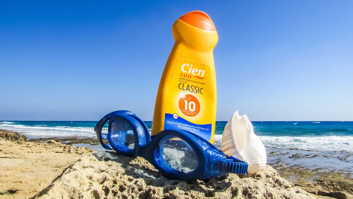 A bottle of sun cream and a pair of swimming googles on a sandy beach