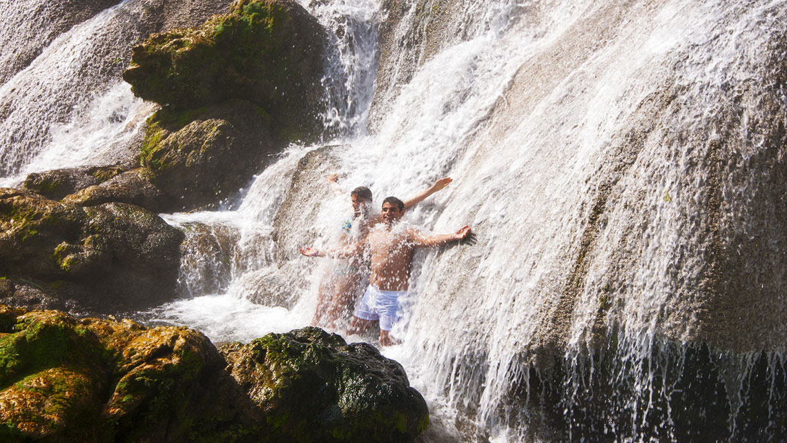 Two young person enjoying a pounding hydromassage against El Nicho foamy-white cascades
