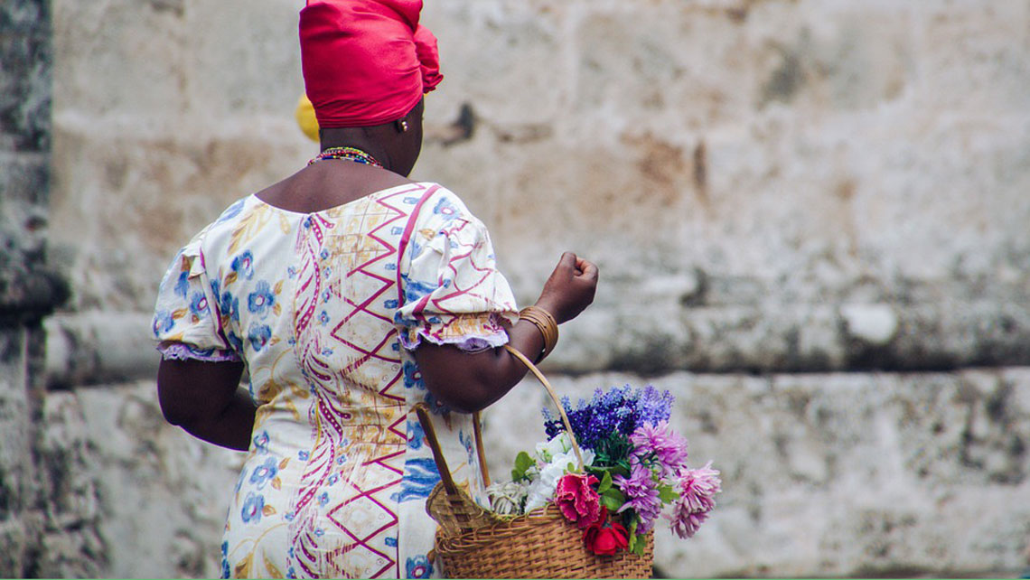 A woman in a traditional cuban dress carrying a basket with flowers