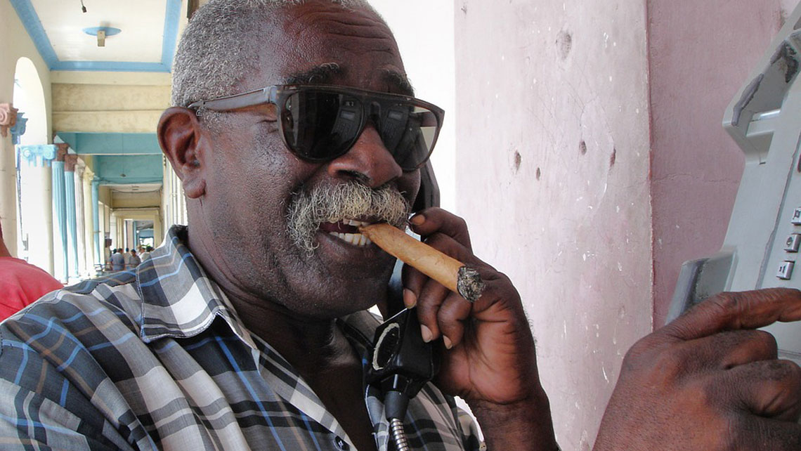 A Cuban smoking a cigar while using a public telephone