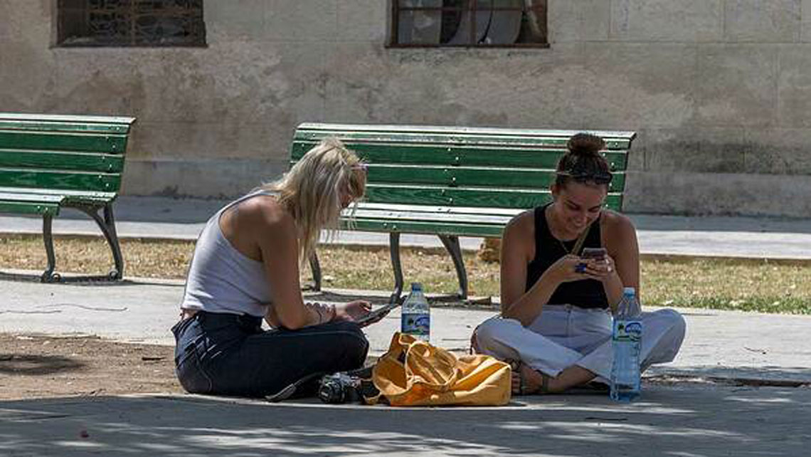 Two young women seating on the ground in a Havana's wifi hot-spot sending messages with their smartphones