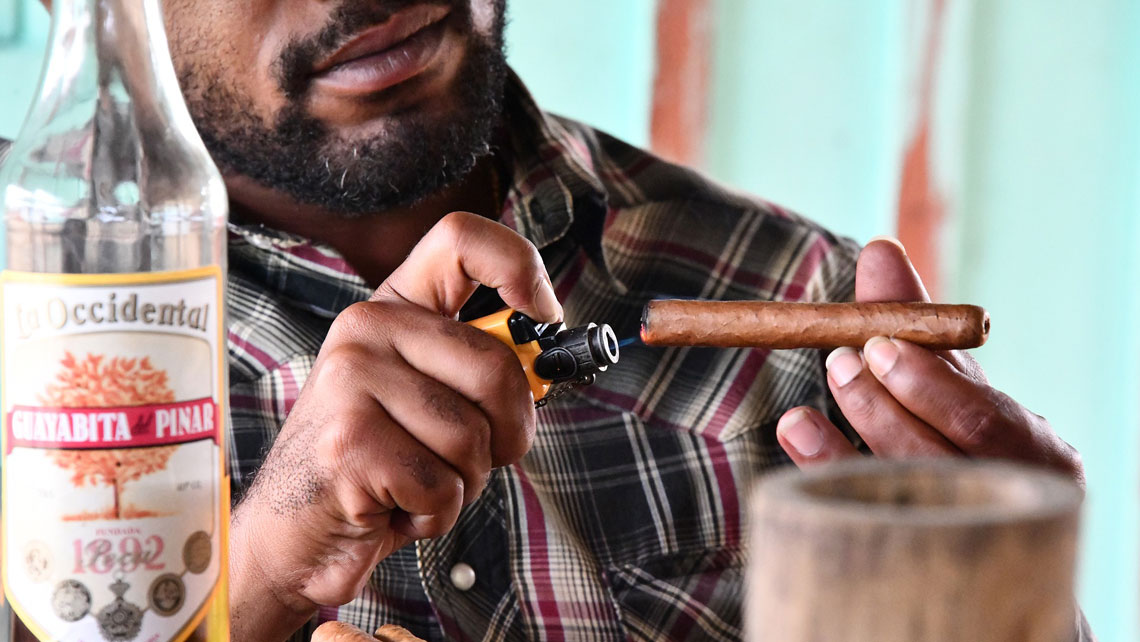 A man lighting a cigar near a bottle of Cuban rum Guayabita del Pinar