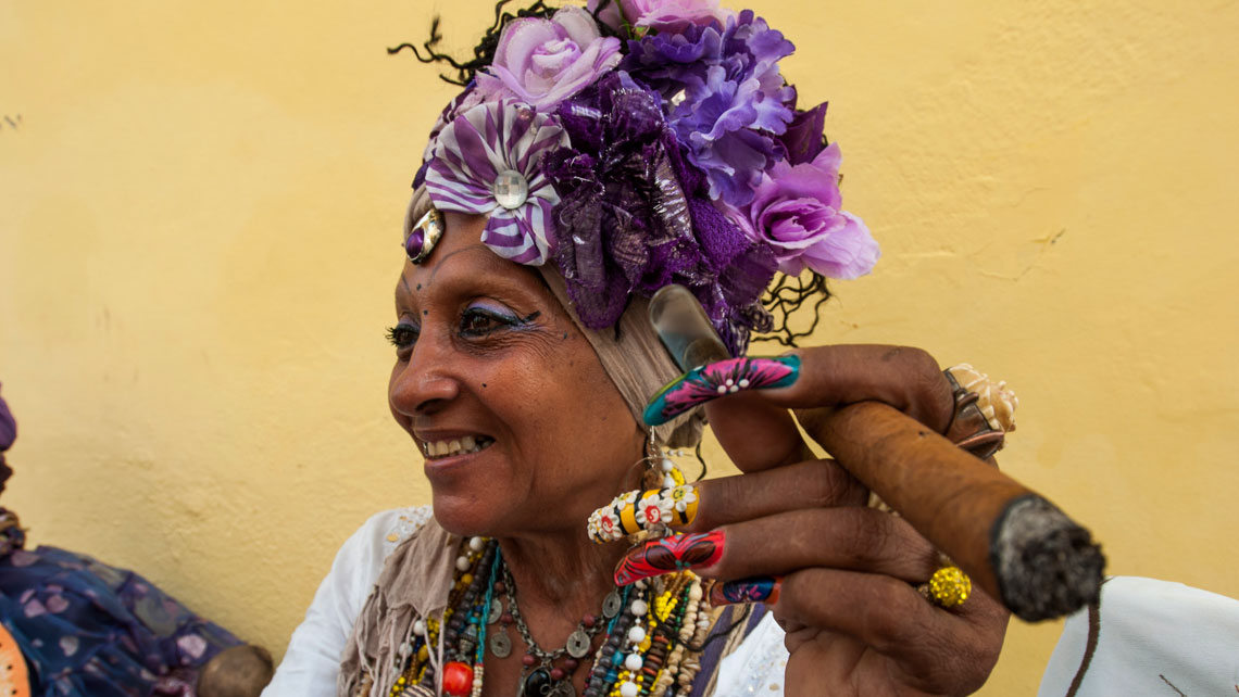 A woman with a cigar and colorful headpiece is seen on the street in Old Havana