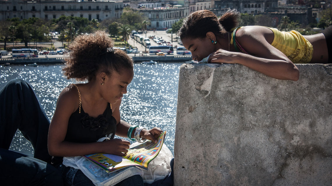 Two young Cuban girls reading a book on a wall in Havana