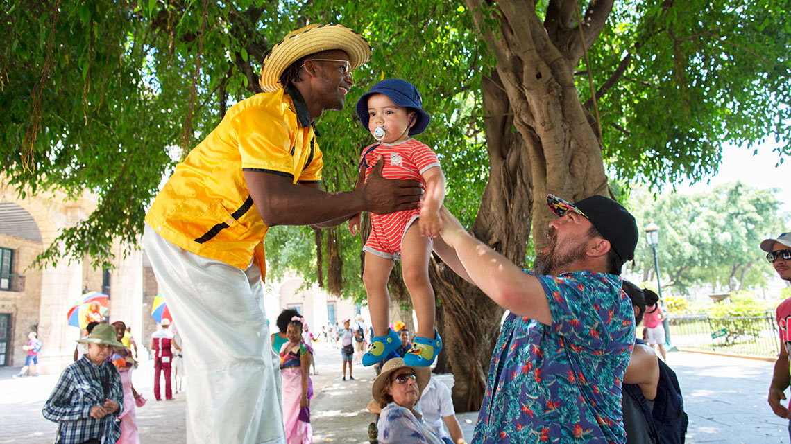 Tourist hands a kid to a local Habanero in Plaza de Armas in Old Havana